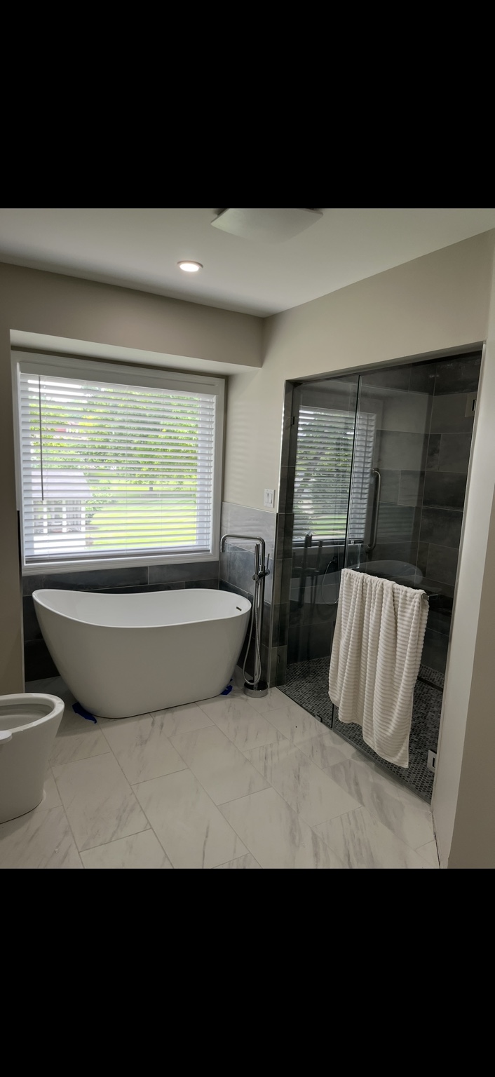 Finished bathroom with a freestanding bathtub, tiled shower and large window